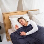 Een persoon die ontspannen in bed ligt met verschillende slaaphulpmiddelen rondom zich, zoals een slaapmasker en kussens.
